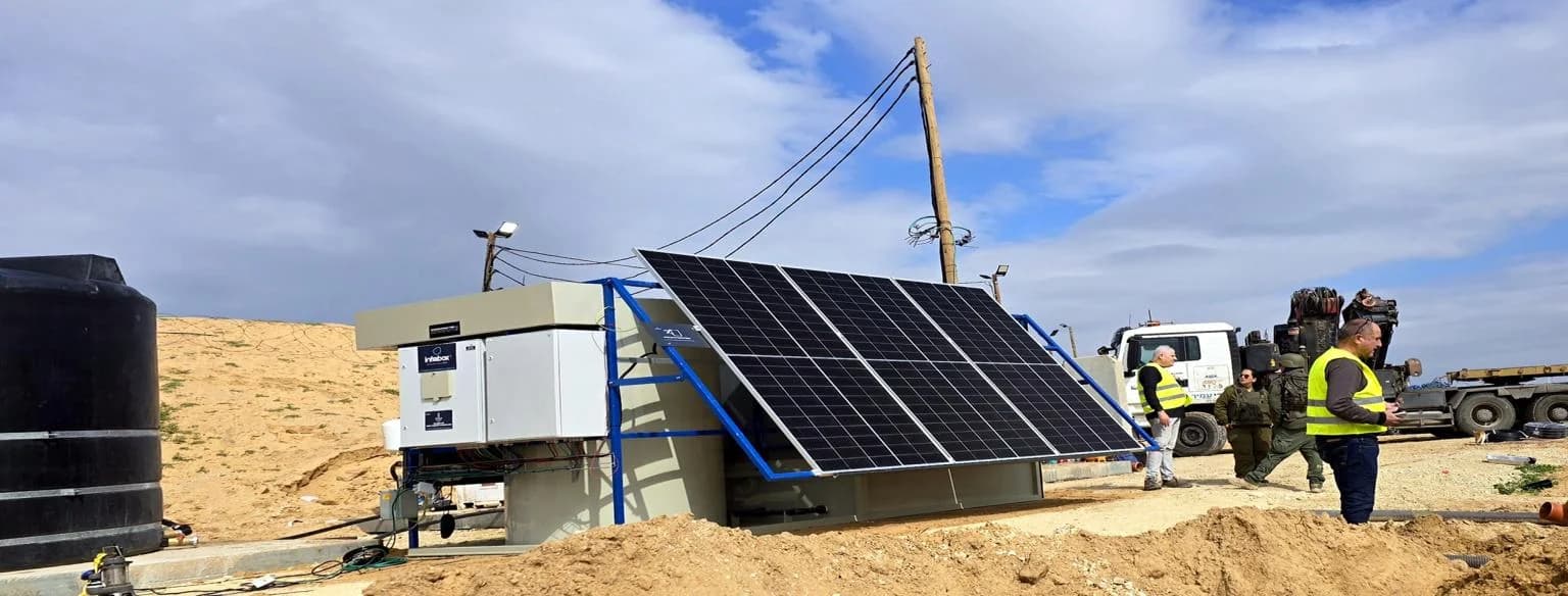 An INFRABOX treatment unit, its blue-framed solar array and the concrete pad on a graded desert site, with overhead lines behind.