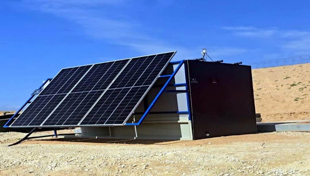 A blue-framed solar array tilted toward the sun beside a black INFRABOX unit