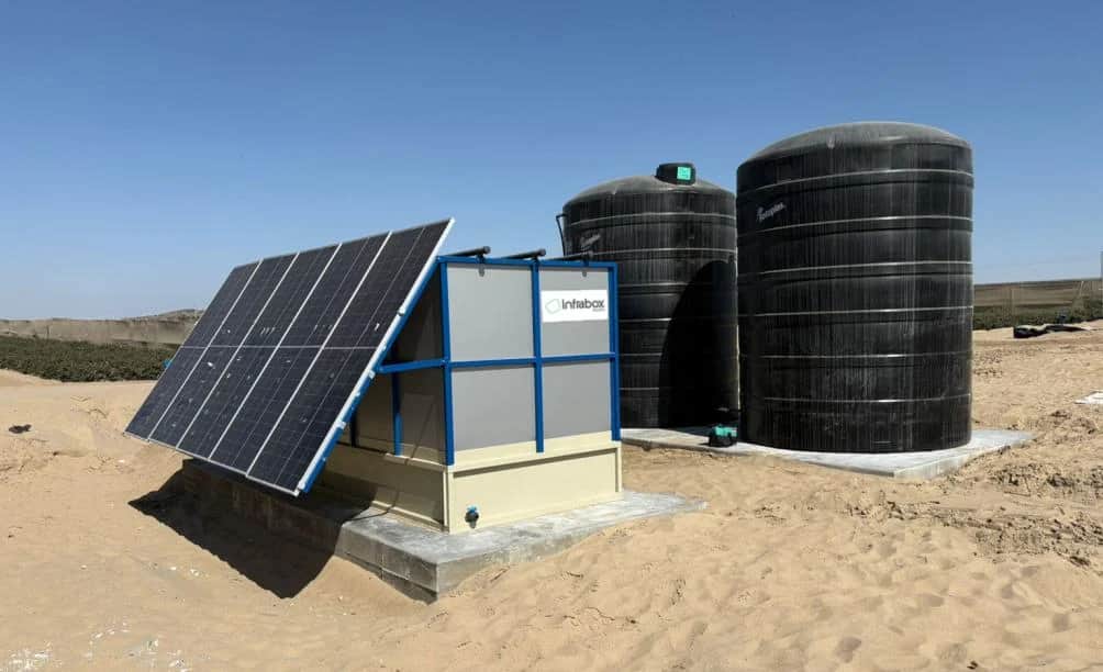 A black INFRABOX treatment unit with two black water tanks and pipework on a concrete pad